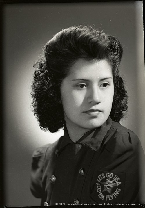 Retrato de mujer joven no identificada, posiblemente mexicoamericana, con peinado estilizado y camisa de uniforme militar con escudo y el lema “Lets go USA, keep em Flying”, en estudio. Posiblemente hija de migrantes que estuvo reclutada en el ejército norteamericano, la fotografía se tomó ya finalizada la guerra, entre octubre y noviembre de 1945. Fresnillo, Zacatecas. Foto: Ricardo Sánchez Ortega. No. inv. 17693. Fototeca del Estado de Zacatecas Pedro Valtierra.